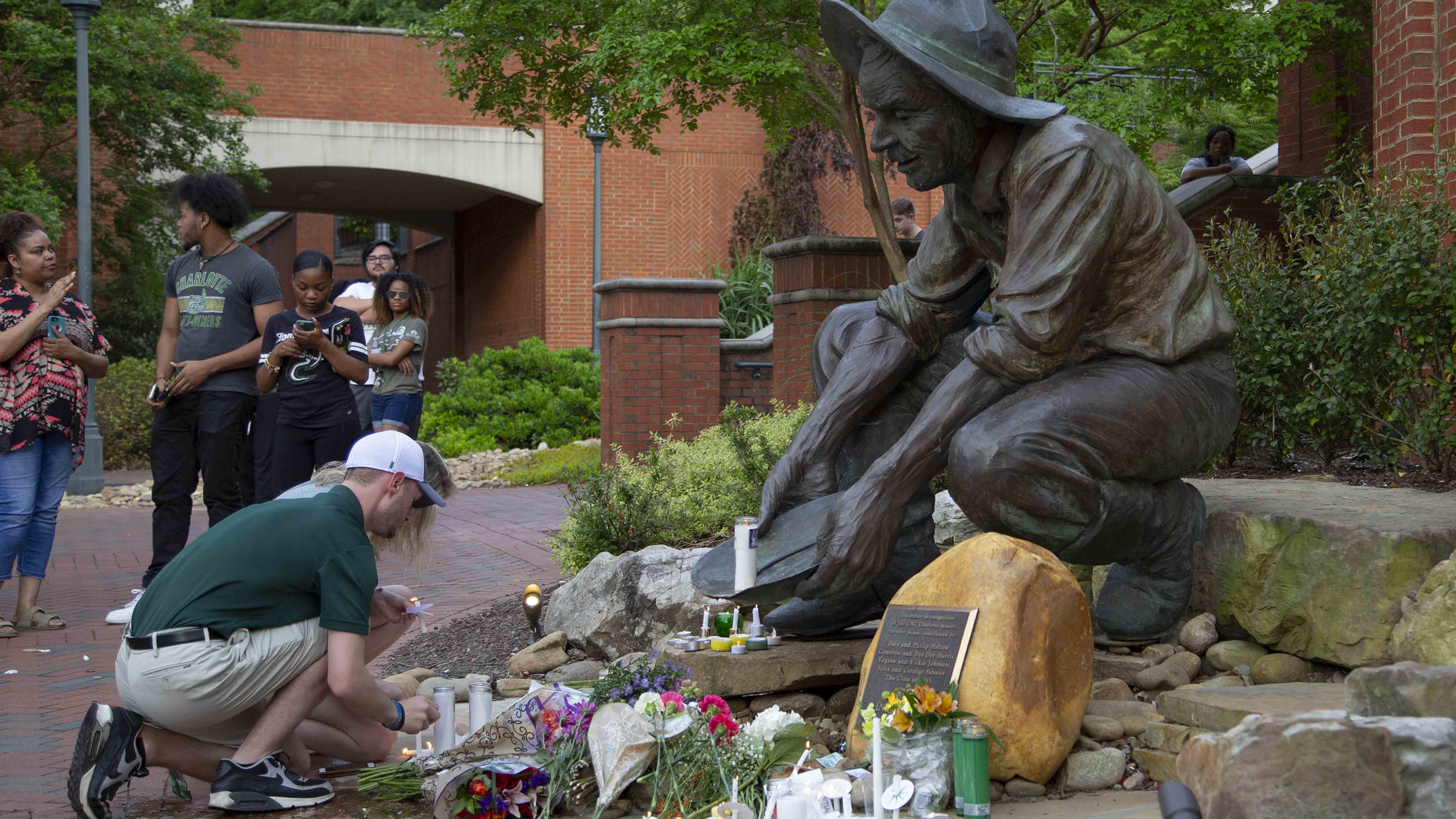 Students placing memorial items and lighting candles at the Niner Miner statue